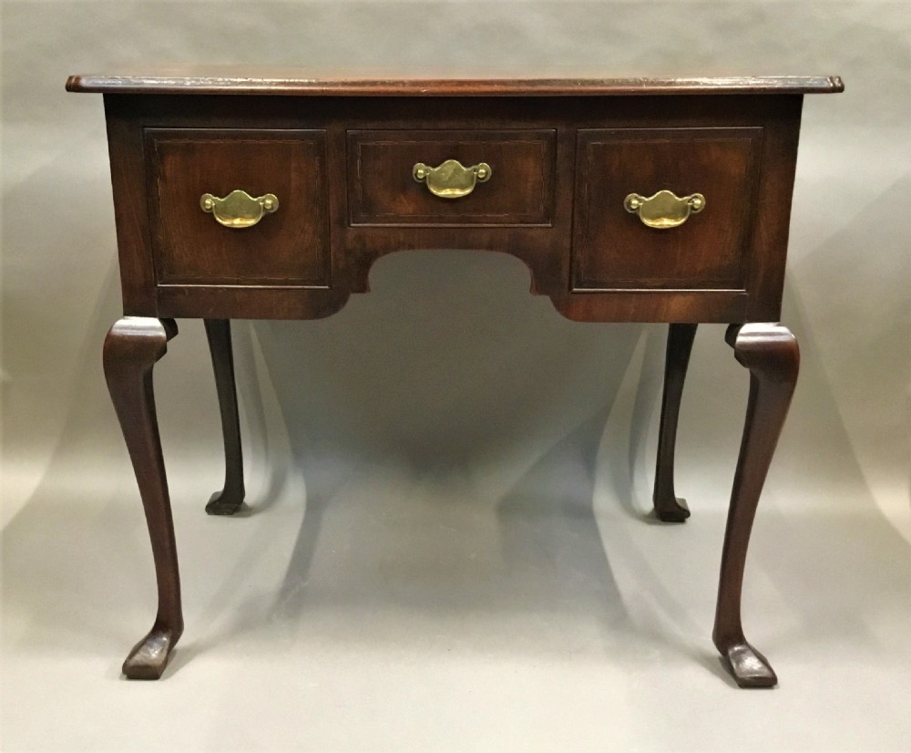 An 18th-century George II mahogany lowboy table featuring three drawers with brass drop handles, a shaped apron, and four cabriole legs with pad feet.