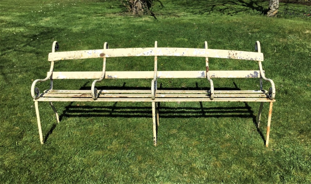 A long nineteenth-century off-white painted iron garden bench featuring scrolled armrests and slatted back supports with weathered patina. View II
