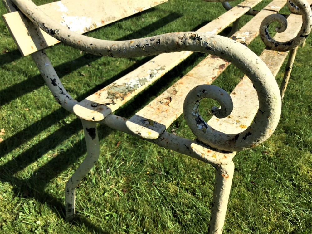 A long nineteenth-century off-white painted iron garden bench featuring scrolled armrests and slatted back supports with weathered patina. View V