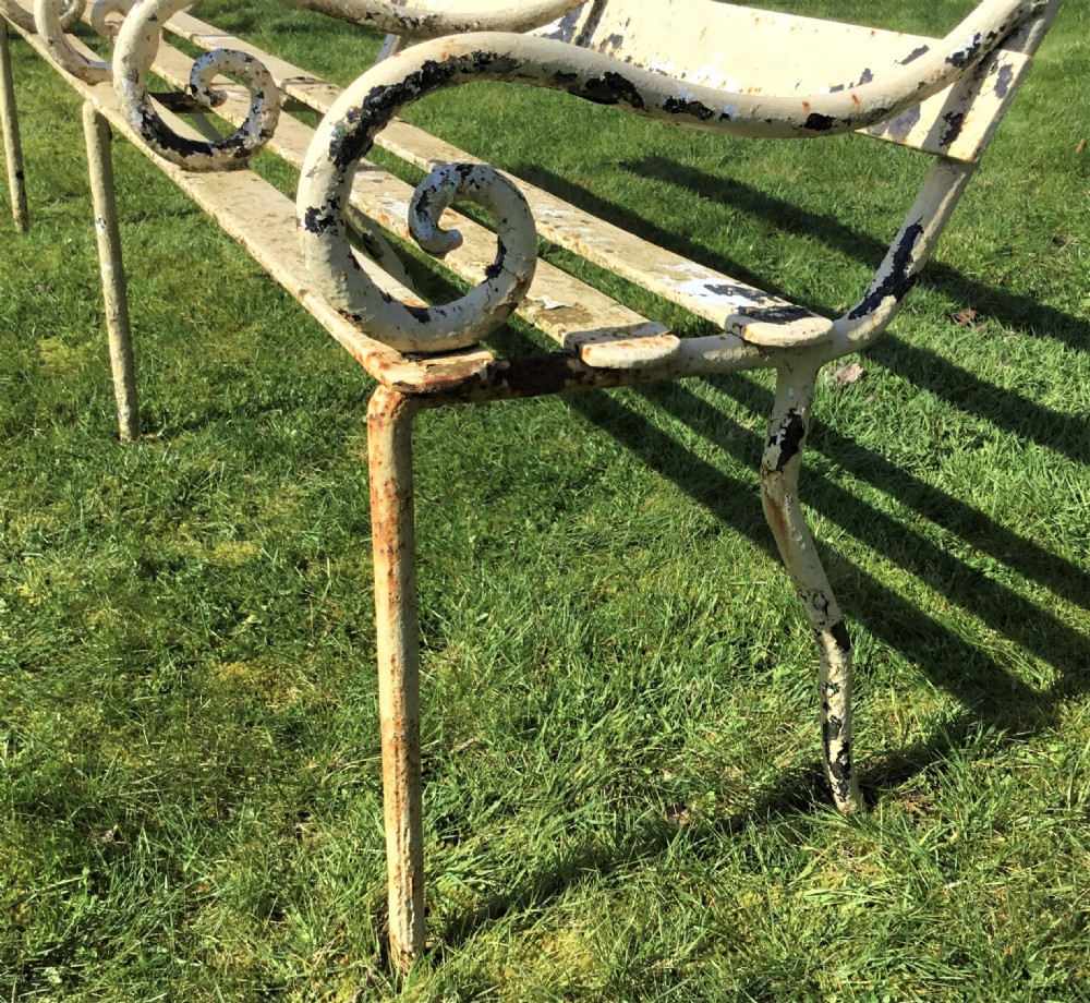 A long nineteenth-century off-white painted iron garden bench featuring scrolled armrests and slatted back supports with weathered patina. View VI