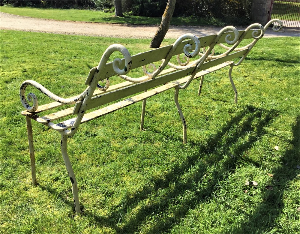 A long nineteenth-century off-white painted iron garden bench featuring scrolled armrests and slatted back supports with weathered patina. View VIII