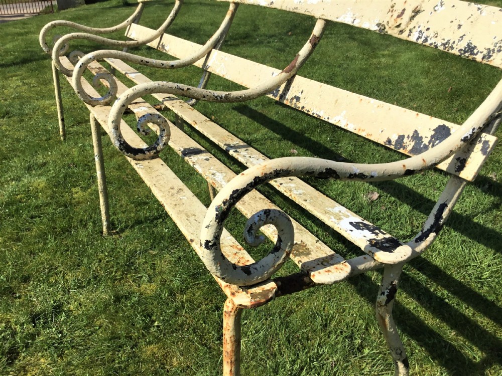 A long nineteenth-century off-white painted iron garden bench featuring scrolled armrests and slatted back supports with weathered patina. View IX
