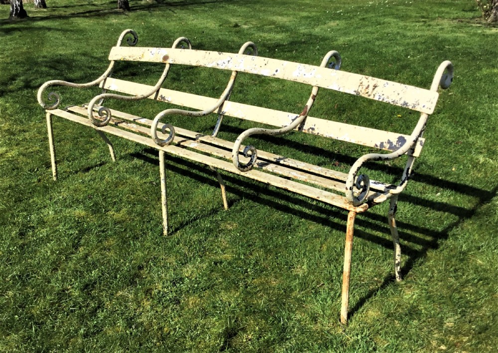 A long nineteenth-century off-white painted iron garden bench featuring scrolled armrests and slatted back supports with weathered patina. View X
