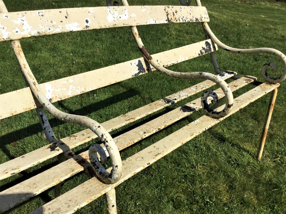 A long nineteenth-century off-white painted iron garden bench featuring scrolled armrests and slatted back supports with weathered patina. View XII