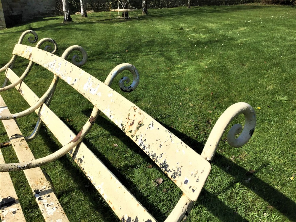 A long nineteenth-century off-white painted iron garden bench featuring scrolled armrests and slatted back supports with weathered patina. View XIII