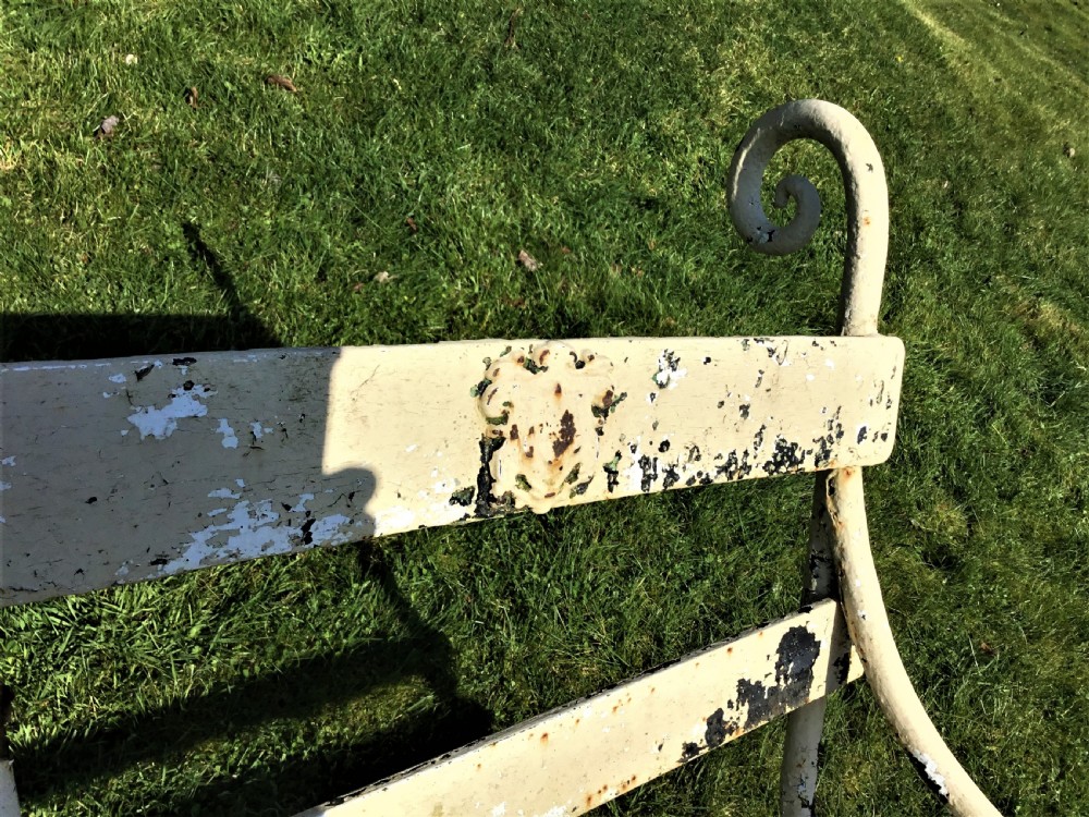 A long nineteenth-century off-white painted iron garden bench featuring scrolled armrests and slatted back supports with weathered patina. View XIV