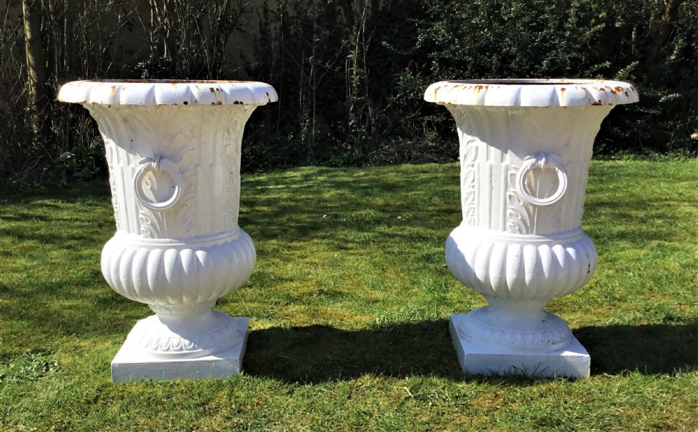 A pair of white painted 19th-century cast iron garden urns featuring fluted rims, side ring handles, gadrooned lower bodies, and square plinth bases. View V