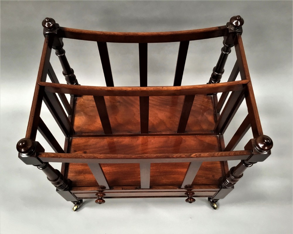 A Regency mahogany dish-top canterbury featuring slatted dividers, turned corner posts with finials, a lower drawer with turned knobs, and legs terminating in brass castors. View V