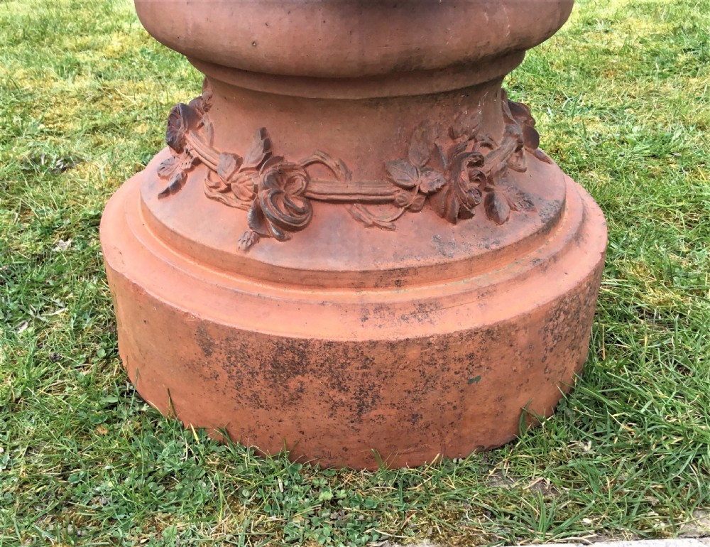 A nineteenth-century terracotta garden urn featuring sculpted mask faces around the body and floral swags on a pedestal base. View IX