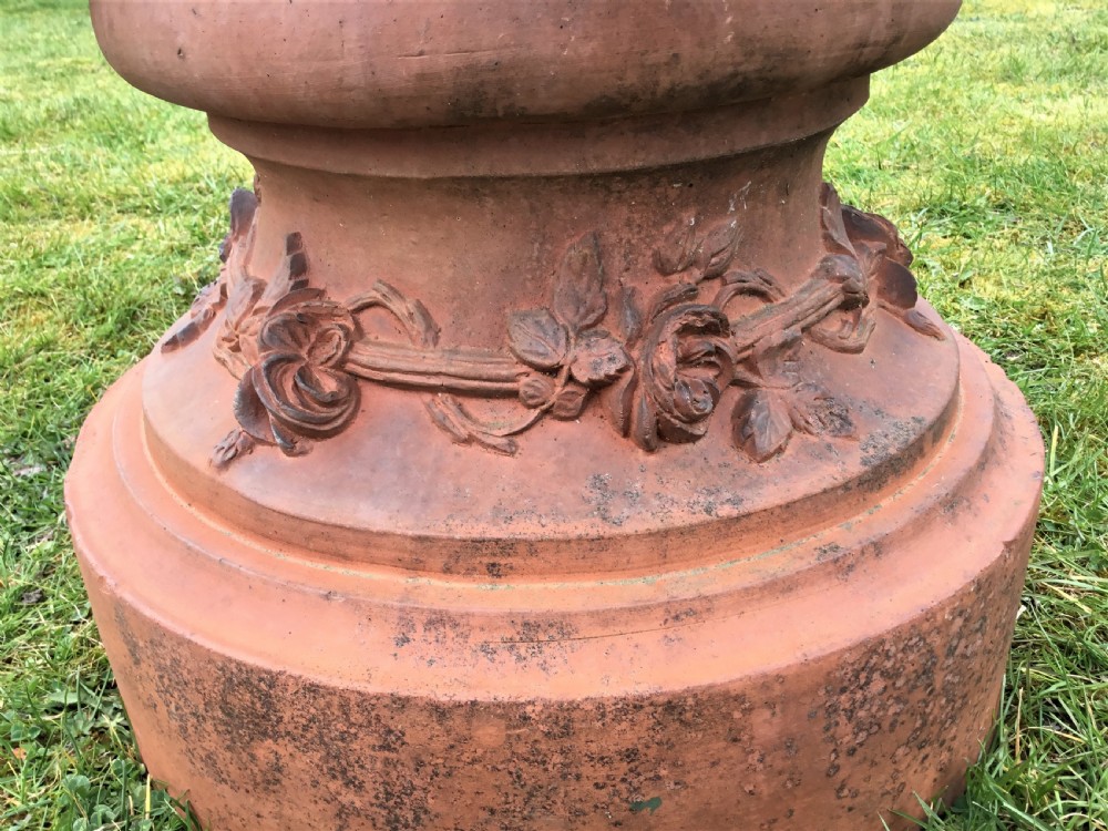 A nineteenth-century terracotta garden urn featuring sculpted mask faces around the body and floral swags on a pedestal base. View X