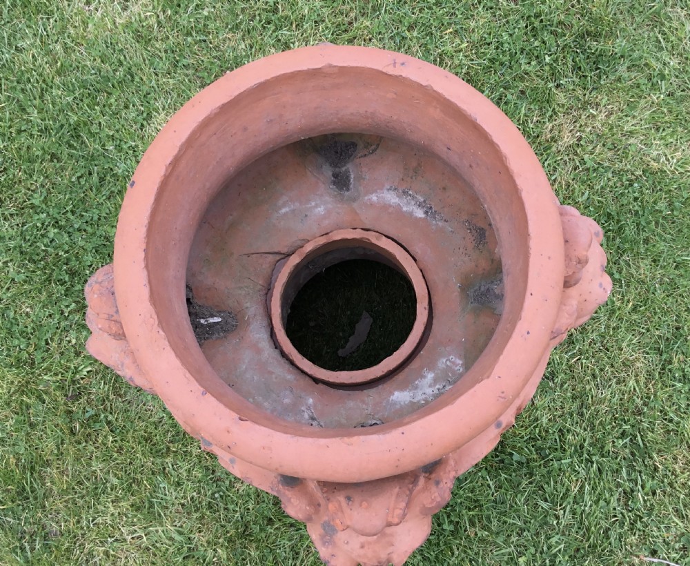 A nineteenth-century terracotta garden urn featuring sculpted mask faces around the body and floral swags on a pedestal base. View XII