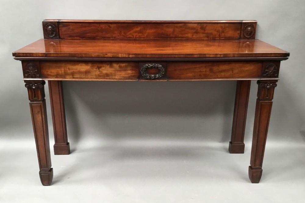 A Regency mahogany side serving table featuring a low upstand with carved rosettes, fluted square tapered legs with ionic capitals, and a flame mahogany apron.
