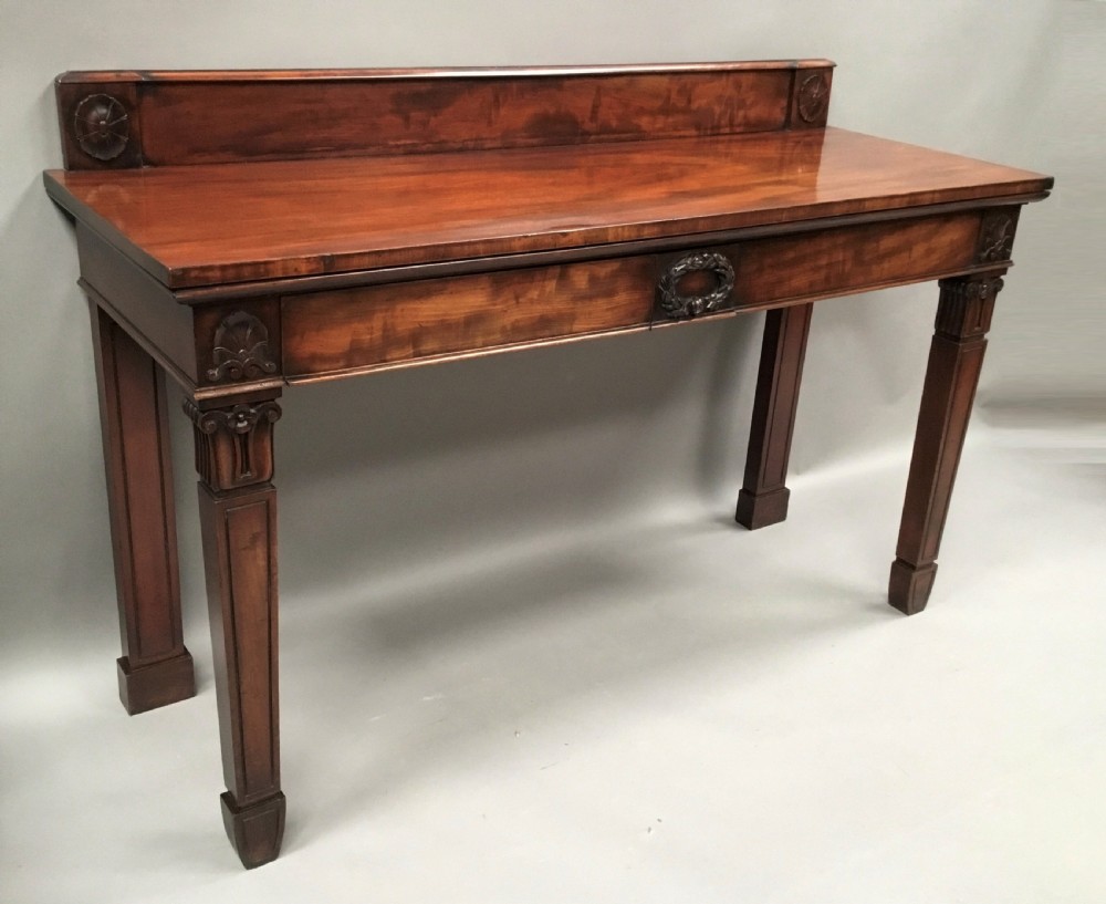 A Regency mahogany side serving table featuring a low upstand with carved rosettes, fluted square tapered legs with ionic capitals, and a flame mahogany apron. View II