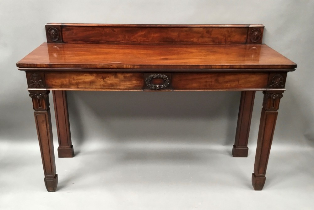 A Regency mahogany side serving table featuring a low upstand with carved rosettes, fluted square tapered legs with ionic capitals, and a flame mahogany apron. View XII