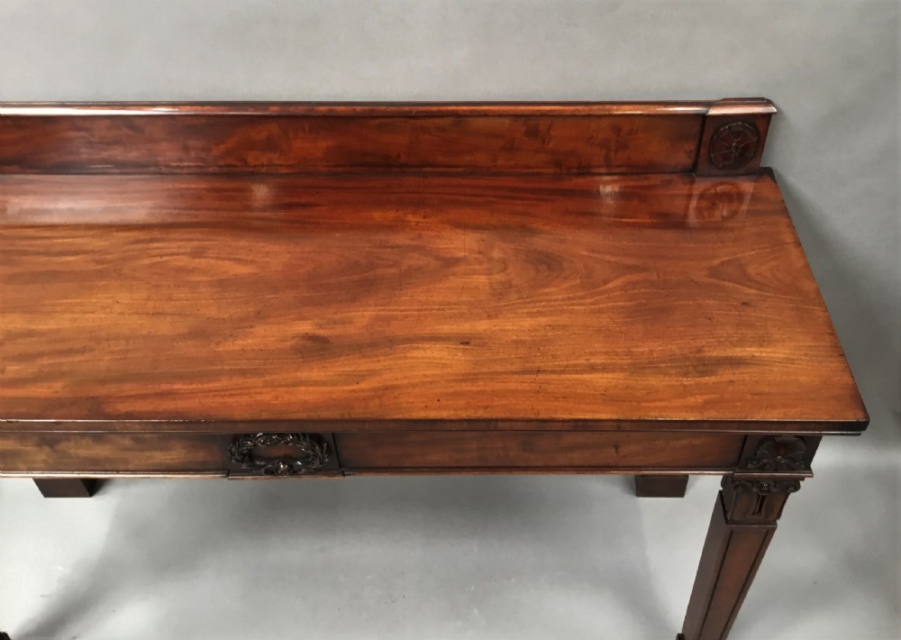 A Regency mahogany side serving table featuring a low upstand with carved rosettes, fluted square tapered legs with ionic capitals, and a flame mahogany apron. View XIII