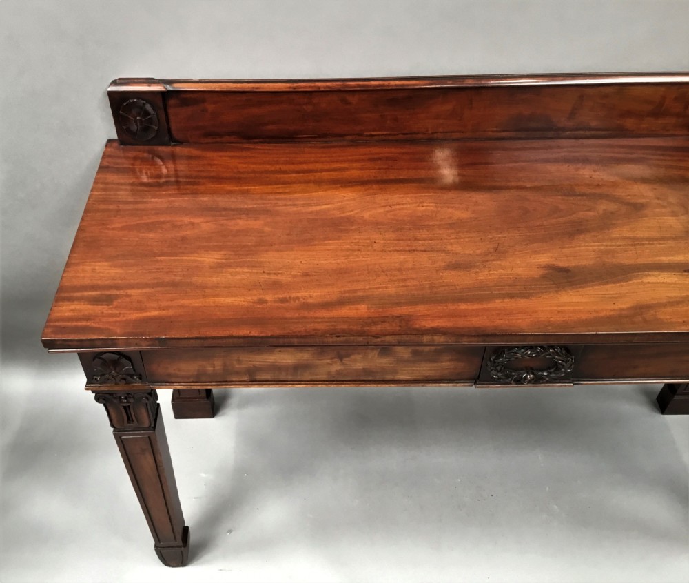 A Regency mahogany side serving table featuring a low upstand with carved rosettes, fluted square tapered legs with ionic capitals, and a flame mahogany apron. View XV