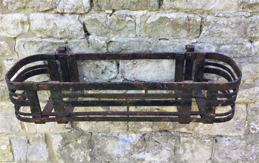 A pair of early 20th-century black wrought iron window boxes with slatted horizontal straps, rounded ends, and top mounting hooks resting on gravel. View II