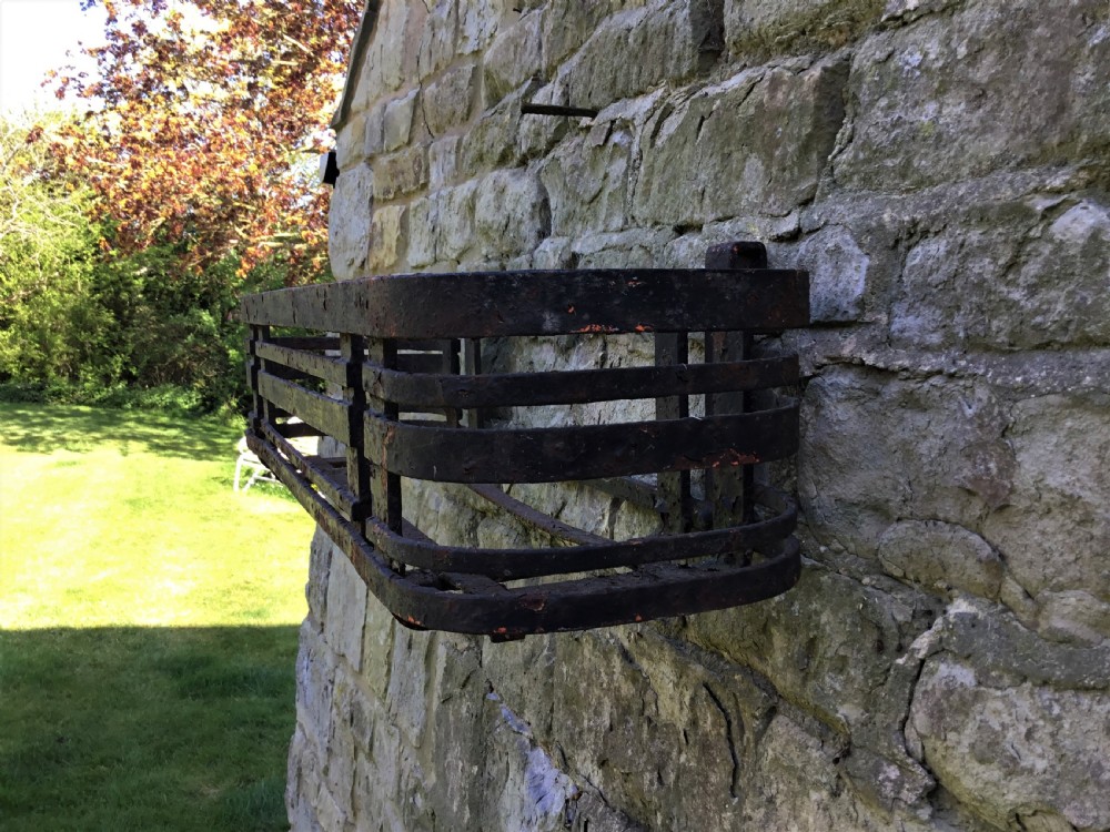 A pair of early 20th-century black wrought iron window boxes with slatted horizontal straps, rounded ends, and top mounting hooks resting on gravel. View VI
