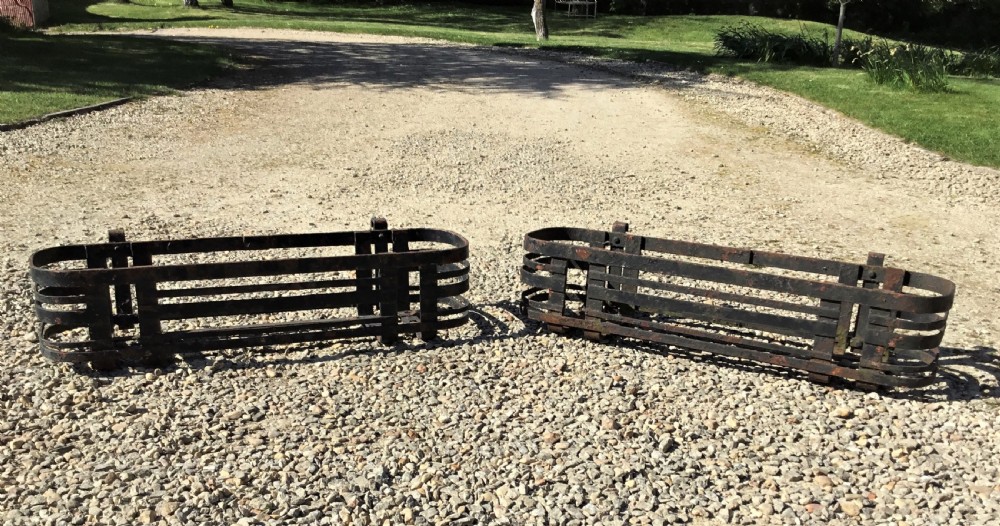 A pair of early 20th-century black wrought iron window boxes with slatted horizontal straps, rounded ends, and top mounting hooks resting on gravel. View VII