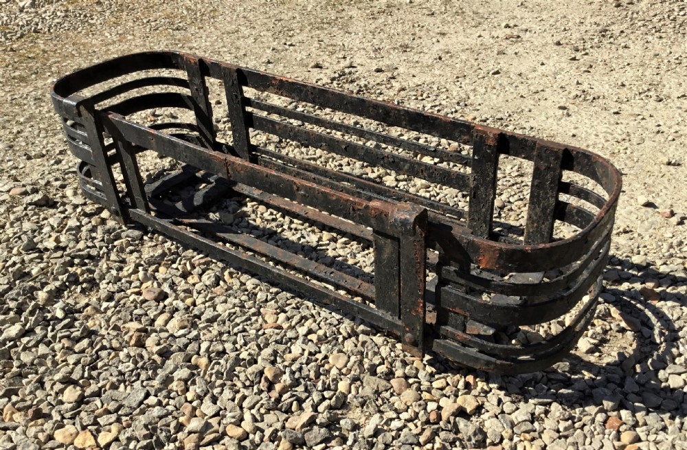 A pair of early 20th-century black wrought iron window boxes with slatted horizontal straps, rounded ends, and top mounting hooks resting on gravel. View X