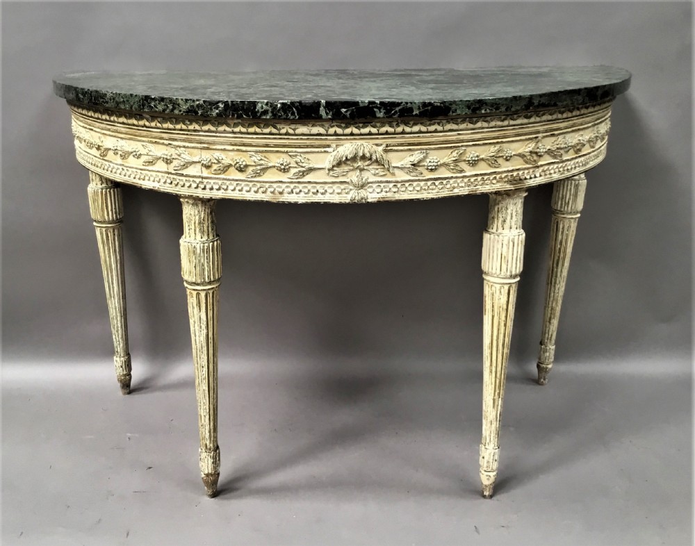 An 18th-century Italian Neoclassical demilune console table featuring an off-white painted timber frame with fluted tapered legs and a dark green marble top.