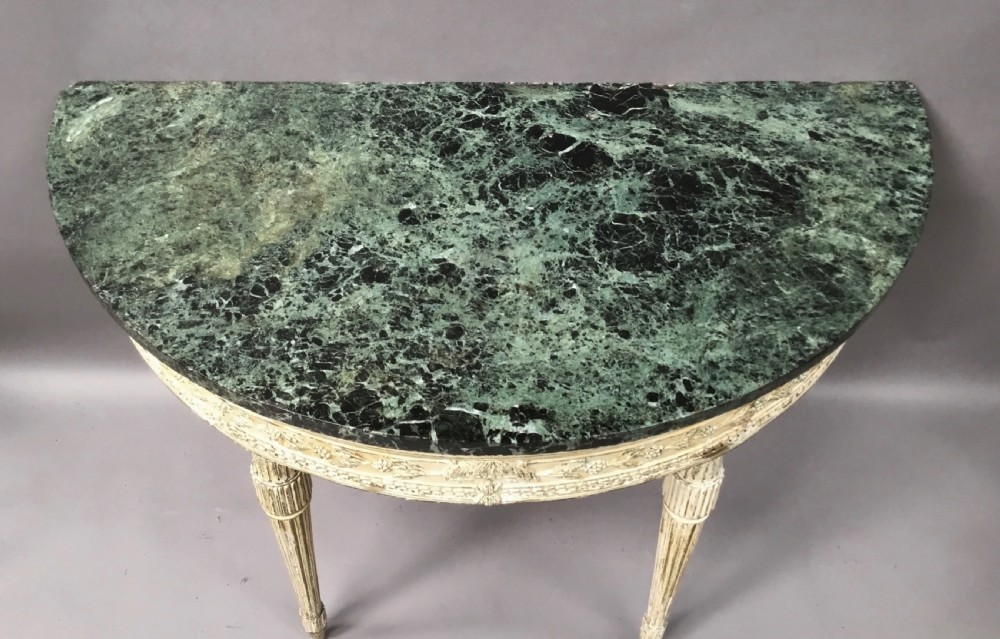 An 18th-century Italian Neoclassical demilune console table featuring an off-white painted timber frame with fluted tapered legs and a dark green marble top. View XVIII