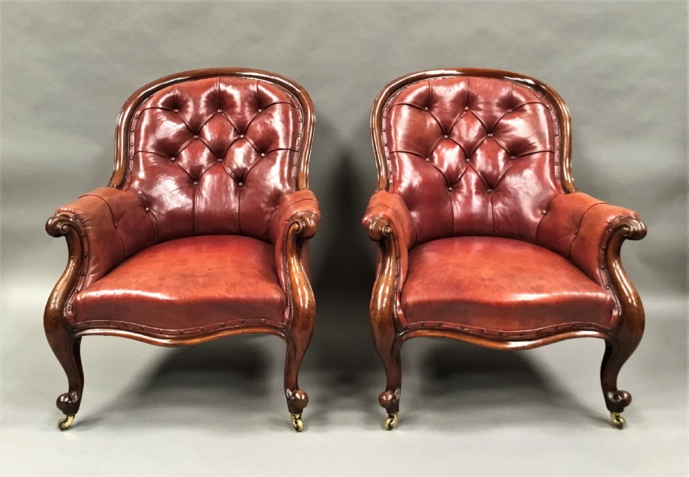 A pair of Victorian mahogany armchairs upholstered in button-backed deep red leather featuring scrolled arms and front cabriole legs on brass castors. View II