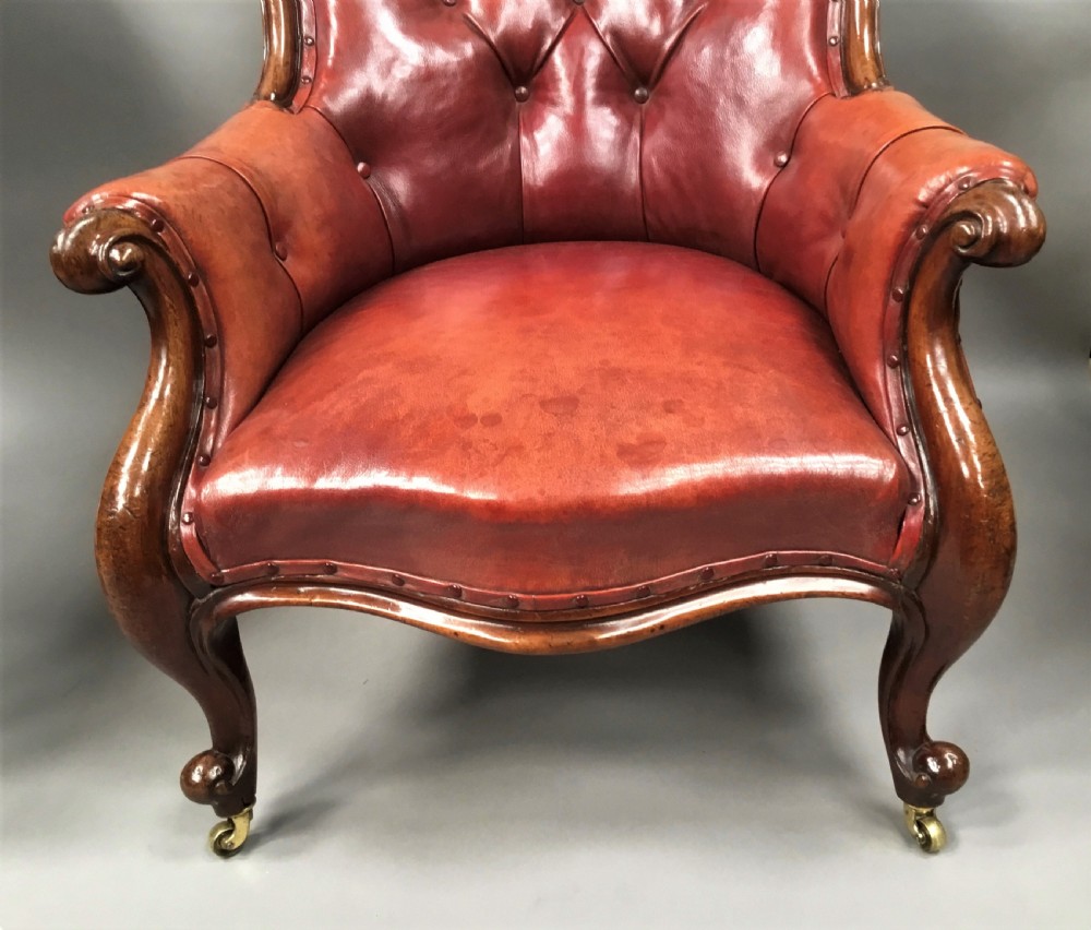 A pair of Victorian mahogany armchairs upholstered in button-backed deep red leather featuring scrolled arms and front cabriole legs on brass castors. View VII