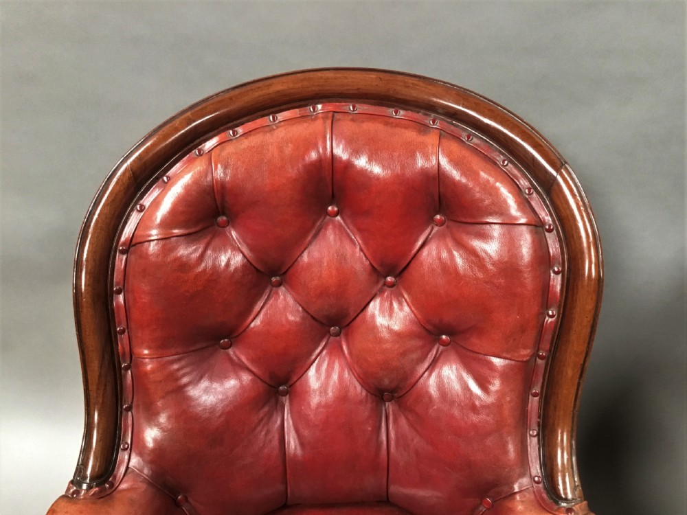 A pair of Victorian mahogany armchairs upholstered in button-backed deep red leather featuring scrolled arms and front cabriole legs on brass castors. View VIII