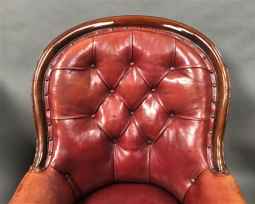 A pair of Victorian mahogany armchairs upholstered in button-backed deep red leather featuring scrolled arms and front cabriole legs on brass castors. View IX