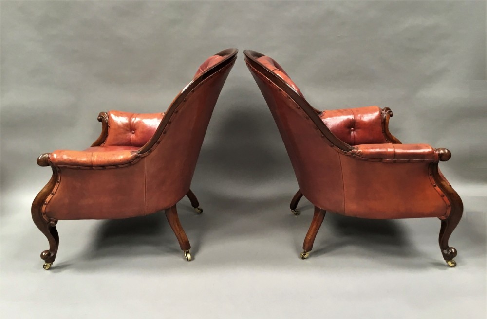 A pair of Victorian mahogany armchairs upholstered in button-backed deep red leather featuring scrolled arms and front cabriole legs on brass castors. View X