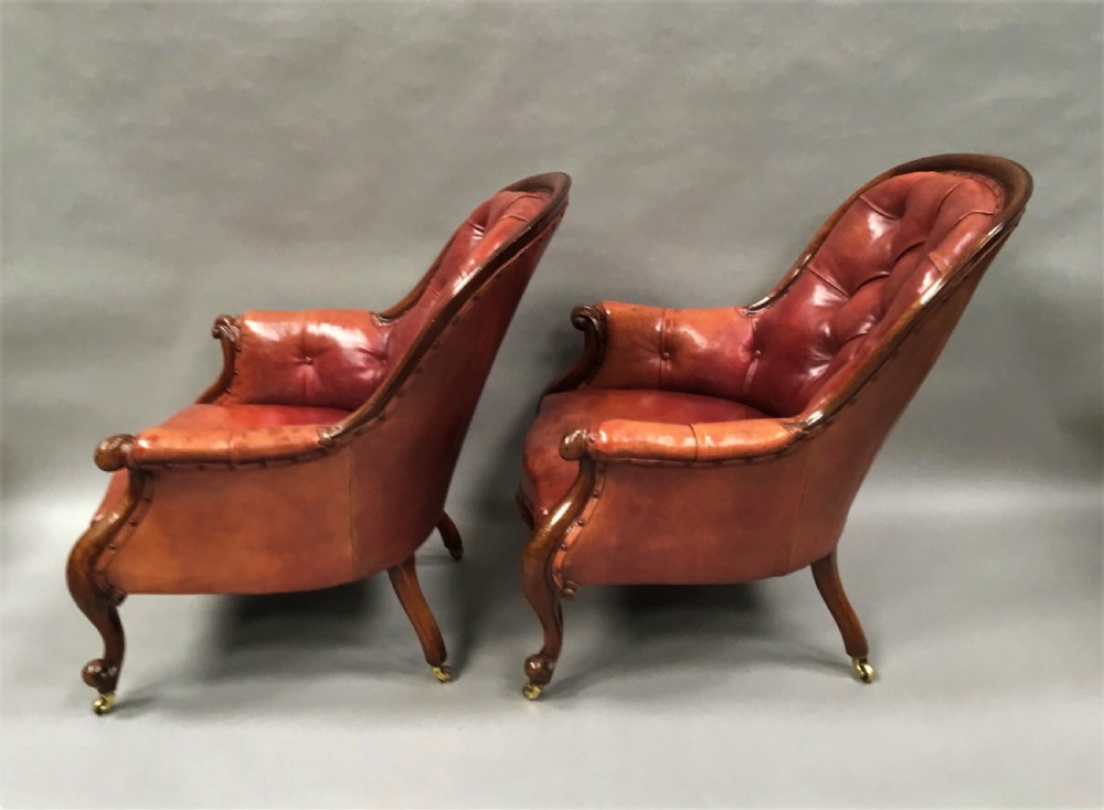 A pair of Victorian mahogany armchairs upholstered in button-backed deep red leather featuring scrolled arms and front cabriole legs on brass castors. View XII