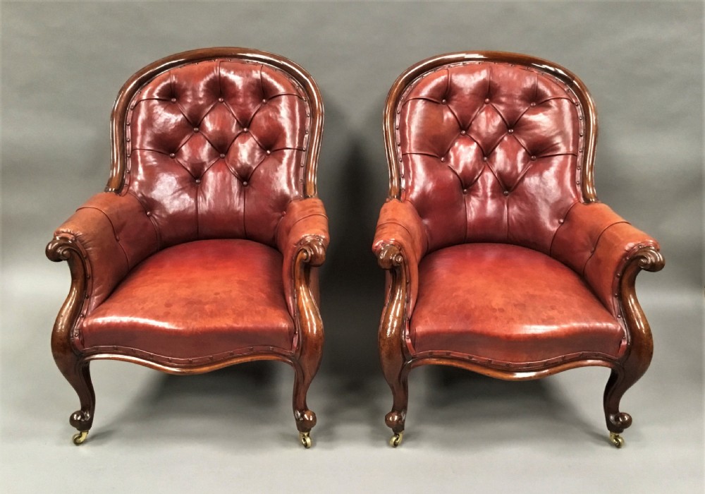 A pair of Victorian mahogany armchairs upholstered in button-backed deep red leather featuring scrolled arms and front cabriole legs on brass castors. View XVIII