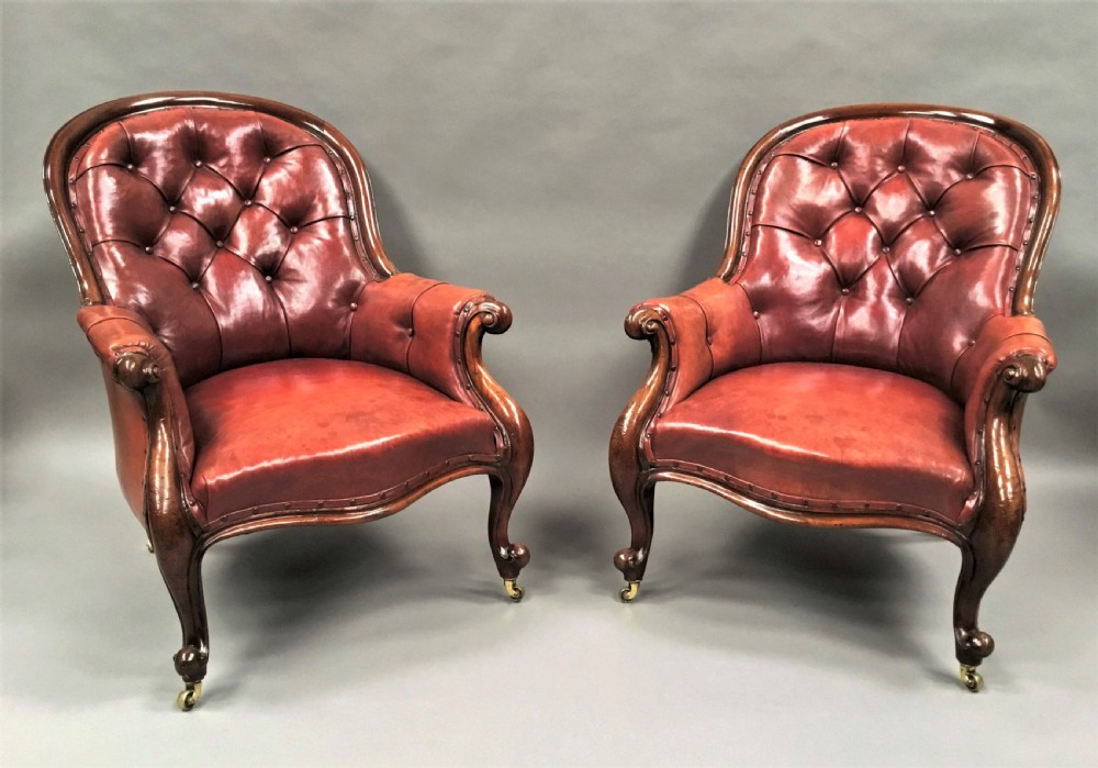 A pair of Victorian mahogany armchairs upholstered in button-backed deep red leather featuring scrolled arms and front cabriole legs on brass castors. View XIX