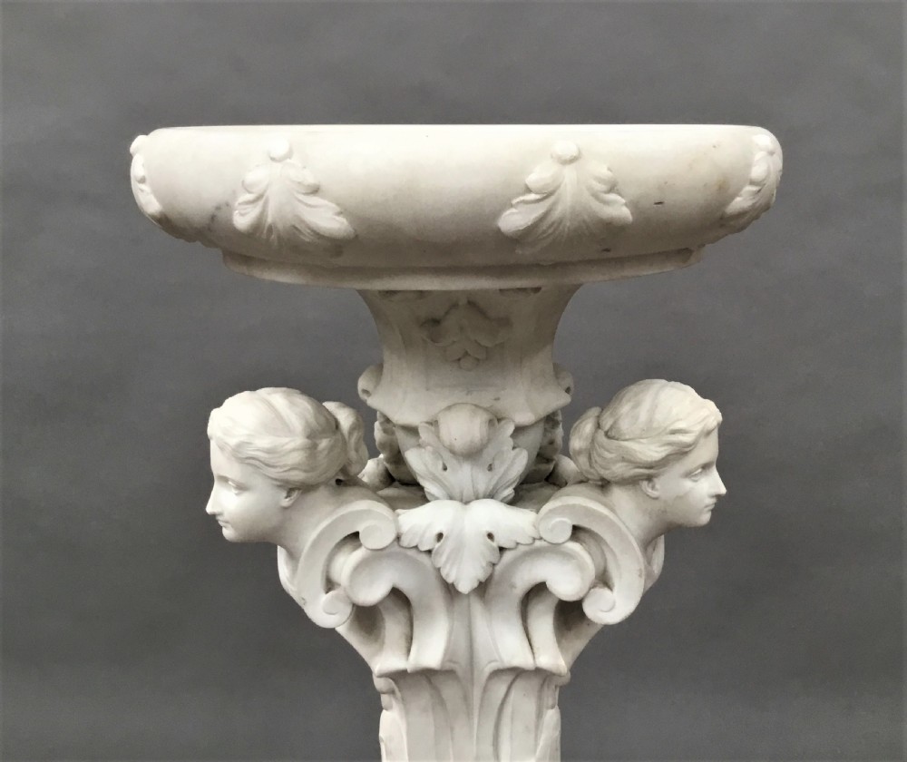 A nineteenth-century carved white Carrara marble torchere stand featuring classical maiden heads, elaborate foliate carvings, a fluted column, and claw feet. View IV