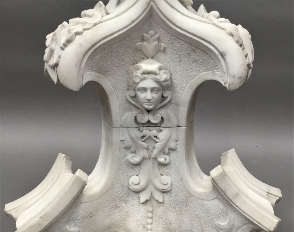 A nineteenth-century carved white Carrara marble torchere stand featuring classical maiden heads, elaborate foliate carvings, a fluted column, and claw feet. View VII