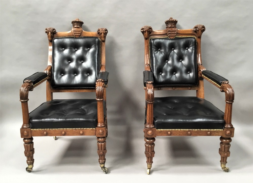 A pair of 19th-century carved oak library armchairs upholstered in buttoned black leather with detailed rams head finials and coronet cresting. View V