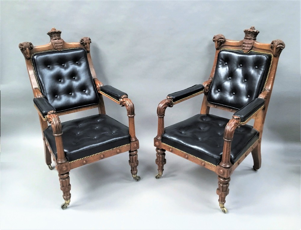 A pair of 19th-century carved oak library armchairs upholstered in buttoned black leather with detailed rams head finials and coronet cresting. View VI