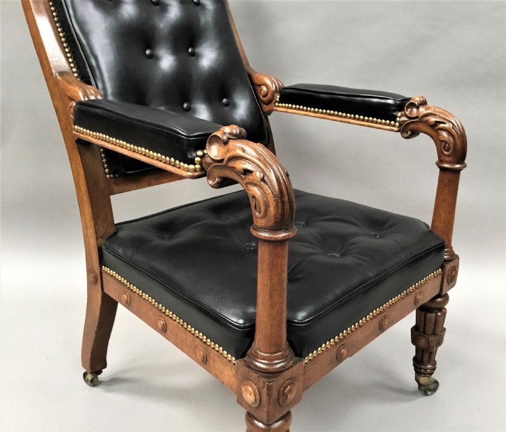 A pair of 19th-century carved oak library armchairs upholstered in buttoned black leather with detailed rams head finials and coronet cresting. View IX