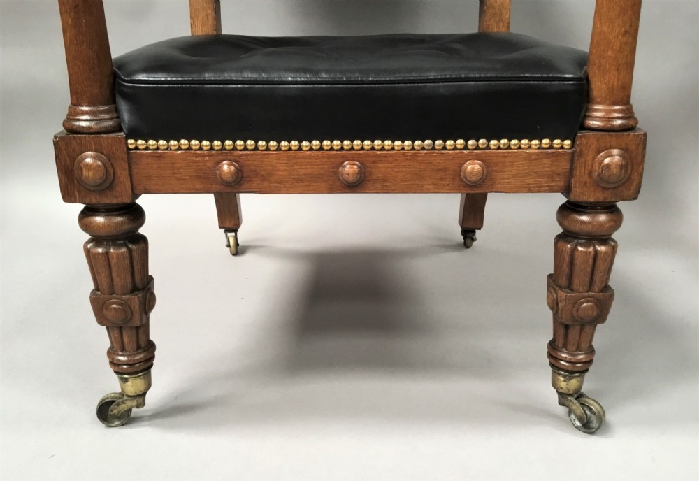 A pair of 19th-century carved oak library armchairs upholstered in buttoned black leather with detailed rams head finials and coronet cresting. View XIII