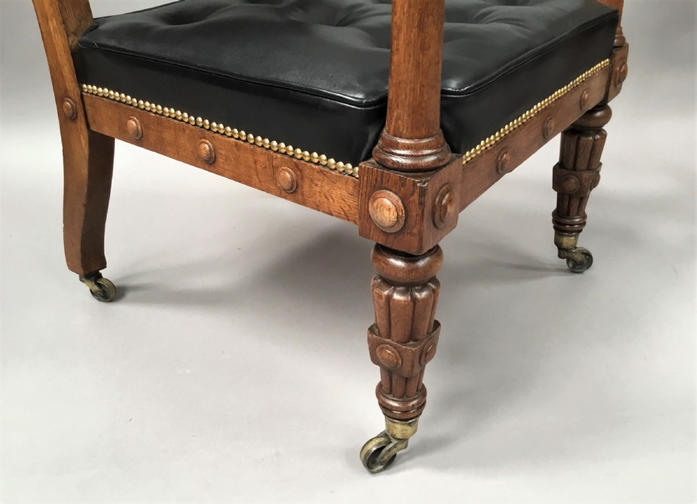 A pair of 19th-century carved oak library armchairs upholstered in buttoned black leather with detailed rams head finials and coronet cresting. View XIV