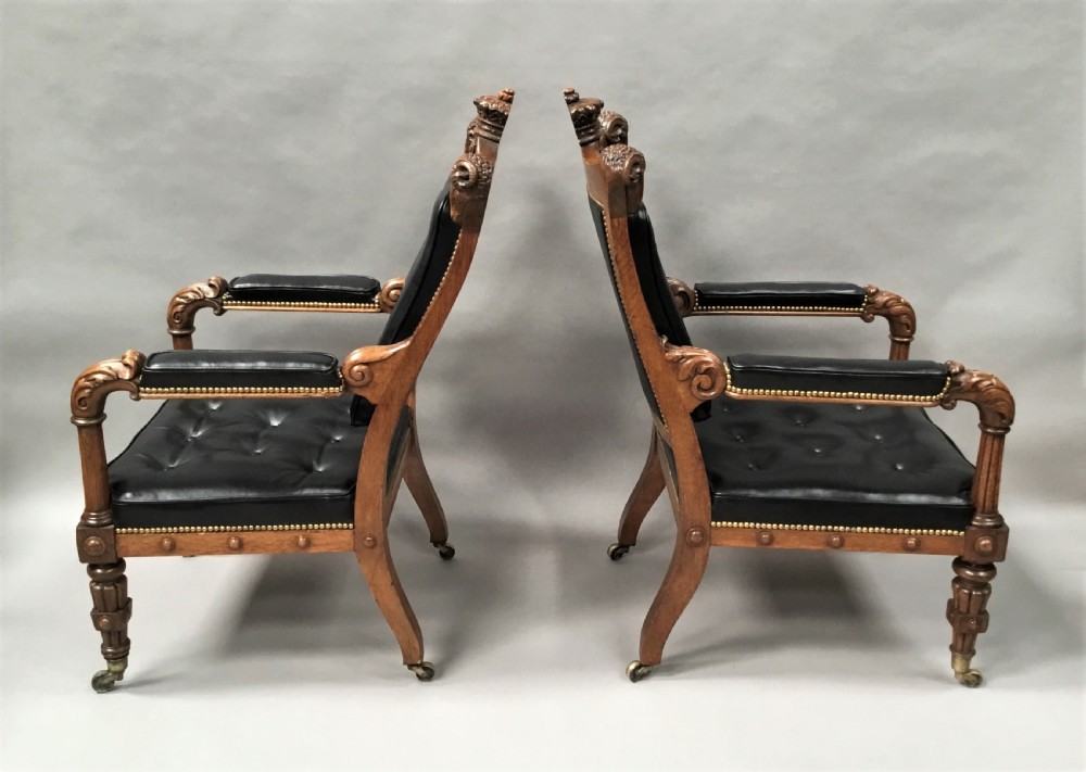 A pair of 19th-century carved oak library armchairs upholstered in buttoned black leather with detailed rams head finials and coronet cresting. View XV