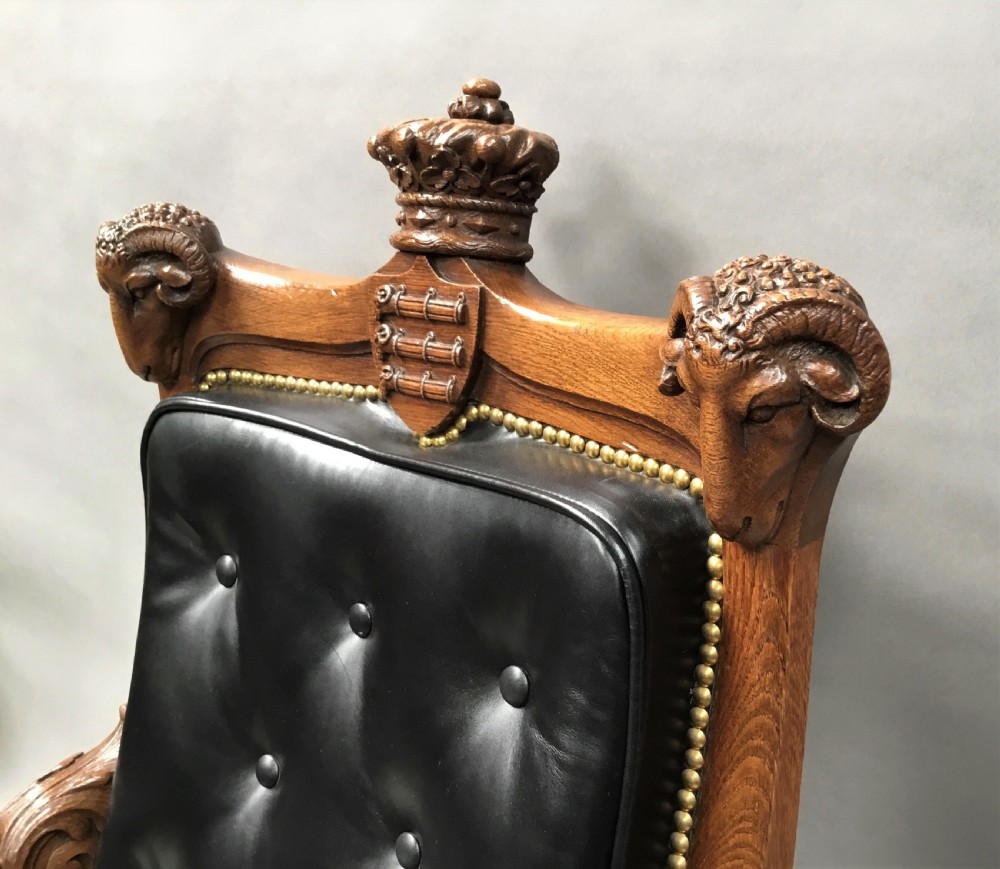 A pair of 19th-century carved oak library armchairs upholstered in buttoned black leather with detailed rams head finials and coronet cresting. View XVII