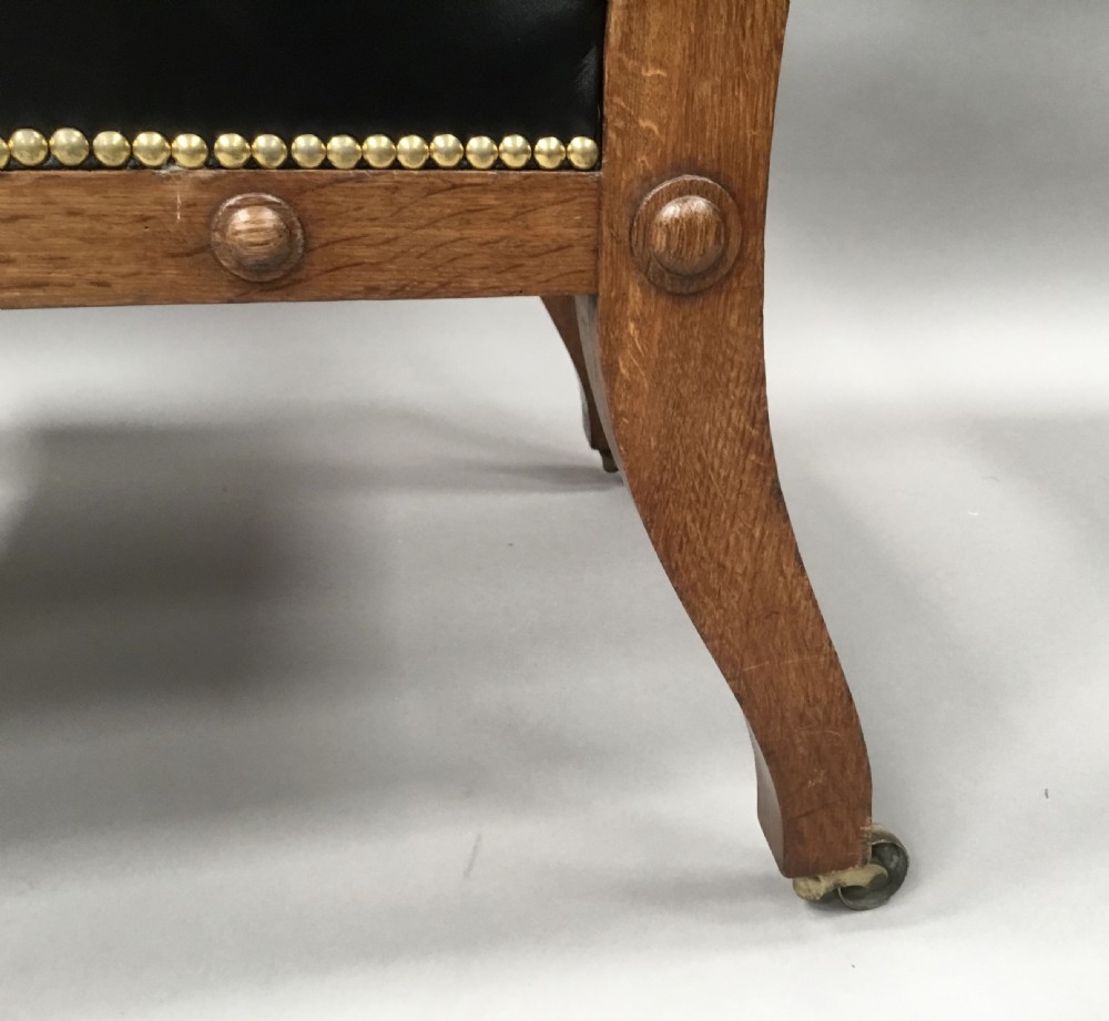 A pair of 19th-century carved oak library armchairs upholstered in buttoned black leather with detailed rams head finials and coronet cresting. View XX