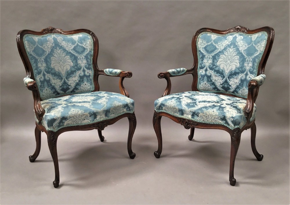 A pair of 18th-century Italian open armchairs featuring carved walnut frames, cabriole legs, and light blue damask pattern upholstery.