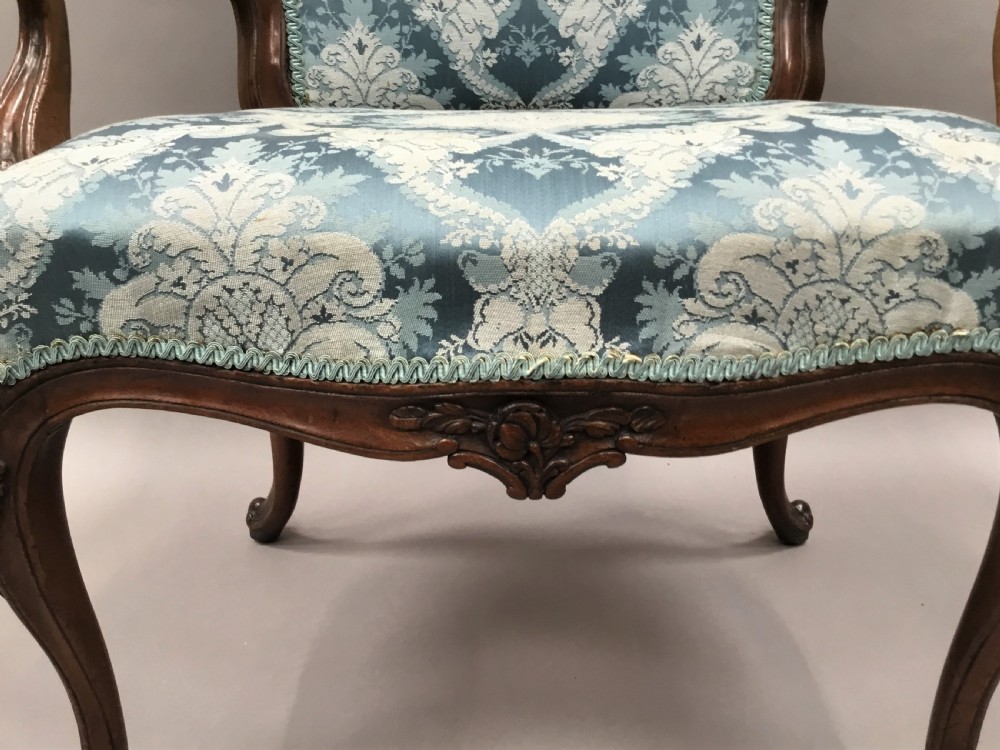 A pair of 18th-century Italian open armchairs featuring carved walnut frames, cabriole legs, and light blue damask pattern upholstery. View XVIII