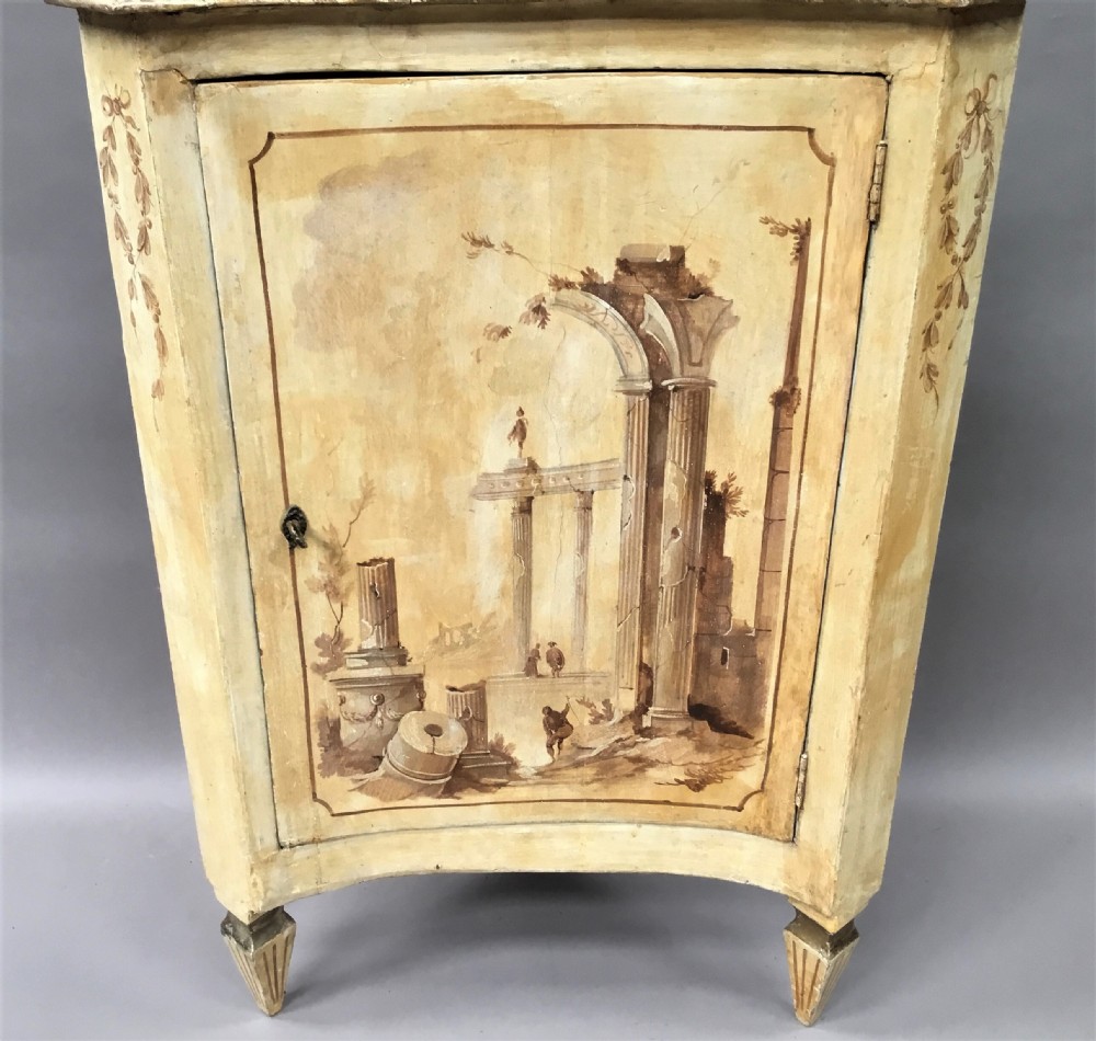 An 18th-century cream-painted Italian standing corner cabinet featuring a curved door decorated with a painted architectural scene and tapered legs. View VII