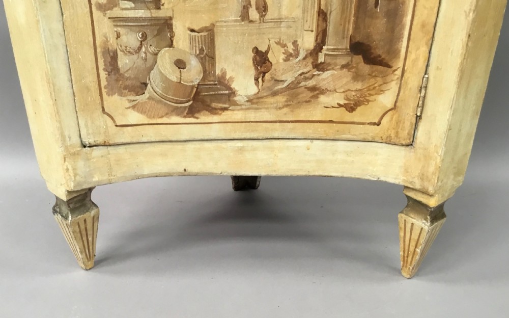 An 18th-century cream-painted Italian standing corner cabinet featuring a curved door decorated with a painted architectural scene and tapered legs. View VIII