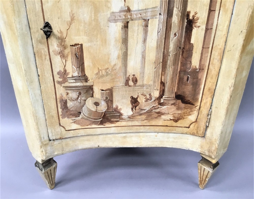 An 18th-century cream-painted Italian standing corner cabinet featuring a curved door decorated with a painted architectural scene and tapered legs. View IX