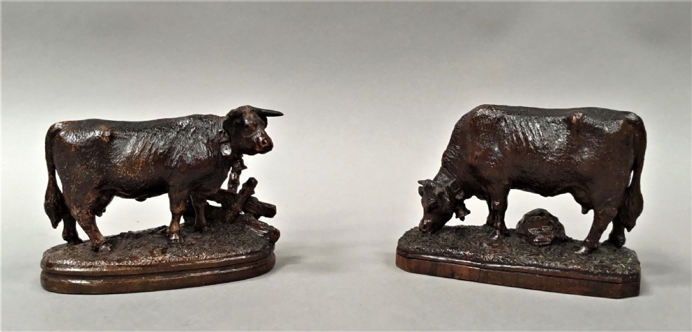 A pair of late nineteenth-century carved dark wood cows mounted on integrated plinths, showing textured coats and bells carved around their necks.